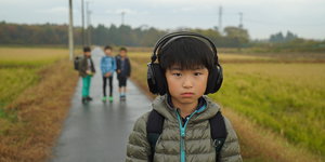 Junge mit Kopfhörer auf Landstraße, weitere Kinder im Hintergrund