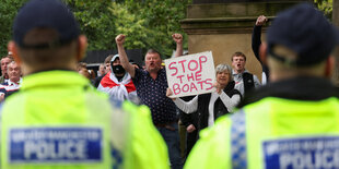 Eine Frau hält bei Protesten ein Pappschild mit der Aufschrift "Stop the boats" in der Hand. Neben ihr stehen weitere Demonstranten.