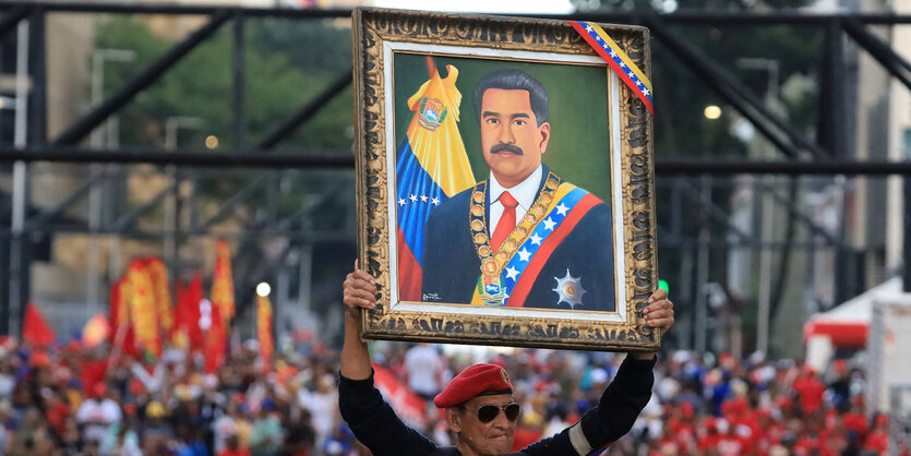 Ein Mann reckt ein gerahmtes Bild von Maduro in die Höhe in einer Menge