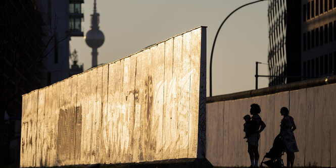 Eine Familie schaut sich an der East Side Gallery im Abendlicht ein Stück der Berliner Mauer an.