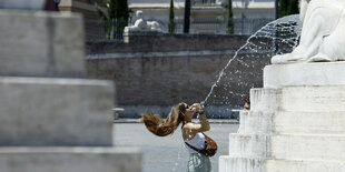 Eine Frau schüttelt ihre Haare an einem Brunnen auf der Piazza del Popolo in der Innenstadt von Rom aus