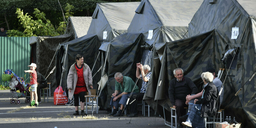 Mehrere evakuierte Menschen sitzen vor Zelten in der Region Kursk