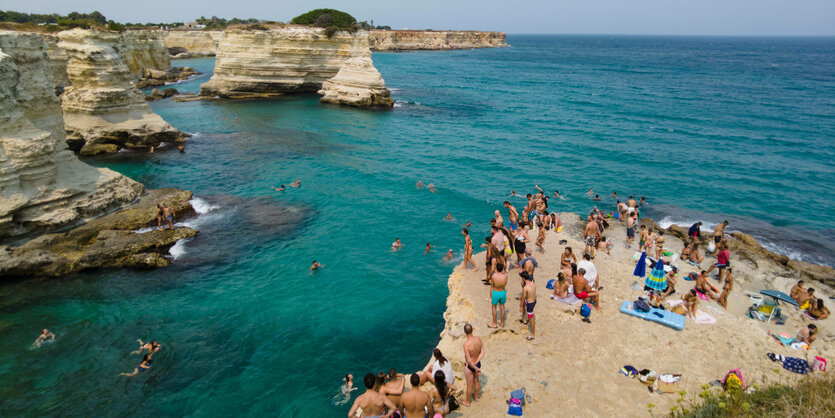 Menschen in Badekleidung stehen auf einem Felsen , einige einige schwimmen im blauen Meer