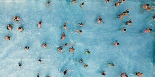 Das Bild zeigt ein Schwimmbadbecken von oben. Einige Menschen schwimmen im Wasser.