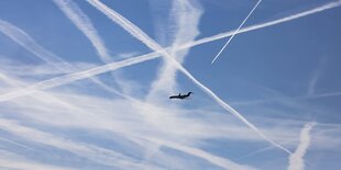 Ein Flugzeug und Kondensstreifen am blauen Himmel