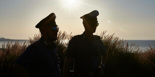 Zwei Carabinieri stehen bei Sonnenuntergang vor einer Küste