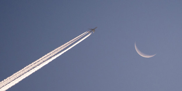 Ein Flugzeug fliegt am Morgenhimmel vor dem Mond vorbei.
