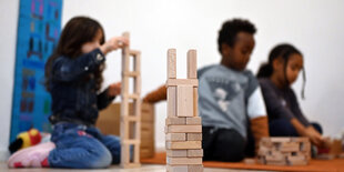 Drei Kinder spielen auf dem Boden mit Holzklötzen