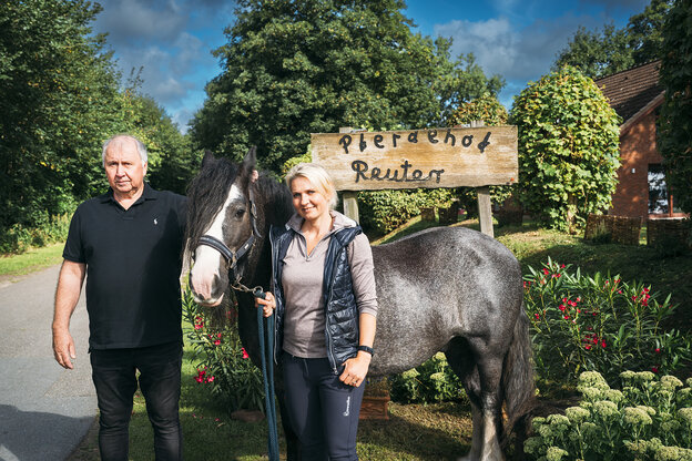 Eine Frau, ein mann und ein Pferd vor einem Holzschild, darauf setht 