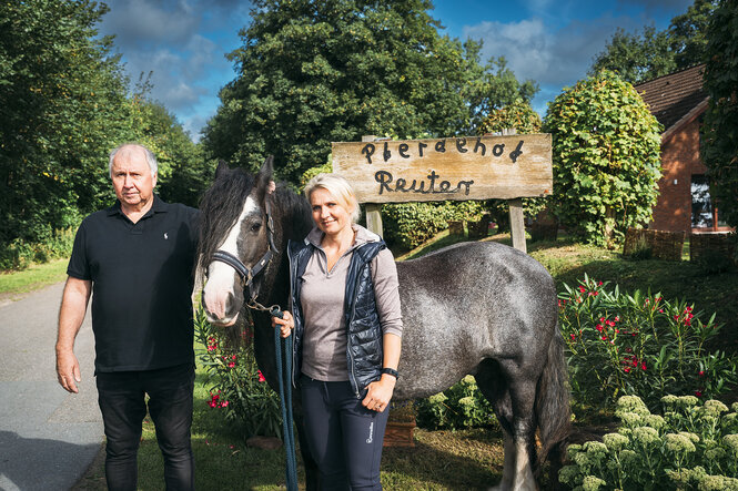 Eine Frau, ein mann und ein Pferd vor einem Holzschild, darauf setht "Ponyhof Reuter"