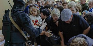 Menschen drängen sich an einem Stand für Hilfslieferungen, der aber nicht so sehen ist, ein maskierter Soldat steht beaffnet vor der Menschenmenge