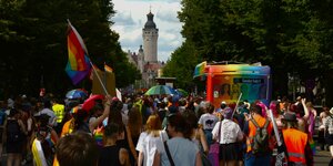 Eine Demonstration mit Regenbogen-Fahnen und bunten Schirmen läuft auf den Turm des Neuen Rathauses in Leipzig zu