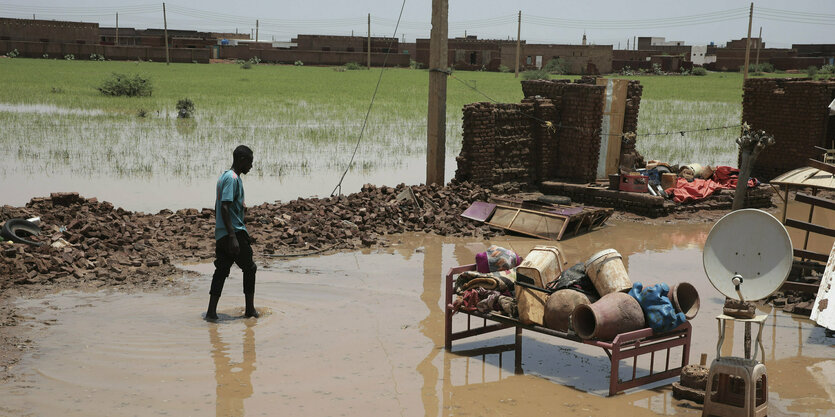 Sudan, Al-Jazirah: Eine Person watet nach schweren Regenfällen durch Hochwasser in der Nähe der Überreste seines Hauses