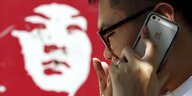 Ein Mensch telefoniert mit einem iPhone und steht dabei vor einem roten, kommunistischen Propagandaplakat