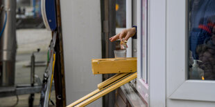 Eine Hand wirft einen 10-Euro Schein in ein Glas, das in einer Holzhalterung steckt