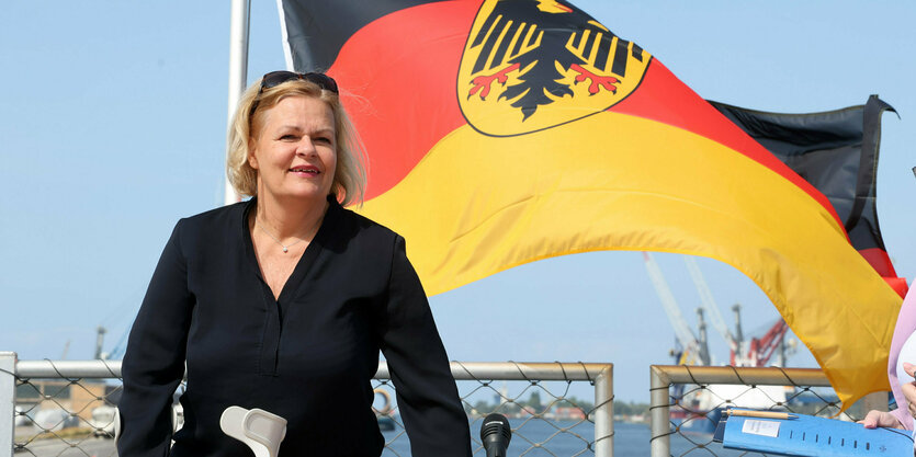 Nancy Faeser steht in Rostock am Meer vor einer Flagge