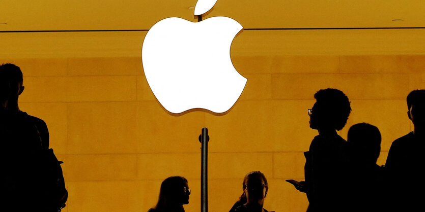 Schattierte Personen-Silhouetten in einem Apple-Store mit Apfel-Logo-Leuchte