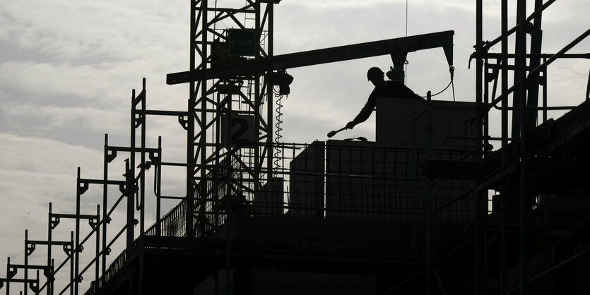 Die Silhouette einer Baustelle ist zu erkennen, ein Bauarbeiter steht auf dem Gerüst.