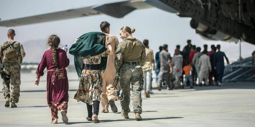 Frauen und Kinder unterwegs zu einem Flugzeug auf dem Rollfeld in Kabul, begleitet von einer us-amerikanischen Soldatin