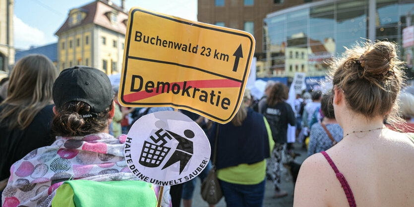 Thüringen, Erfurt: Eine Teilnehmerin hält ein Schild mit der Aufschrift «Buchenwald 23 km», dem durchgestrichenen Schriftzug «demokratie» und einer Figur, die ein Hakenkreuz in einen Mülleimer wirft.