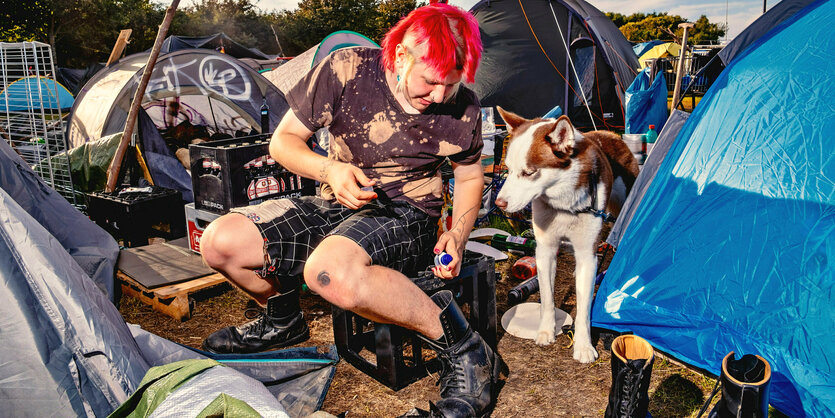 Punk mit roten Haaren und Hund zwischen Zelten