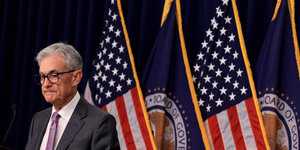 Jerome Powell bei einer Pressekonferenz vor US Flaggen