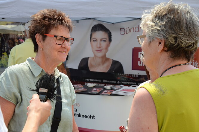 Zwei Frauen unterhalten sich, im Hintergrund ein Plakat mit dem Portrait von Sarah Wagenknecht