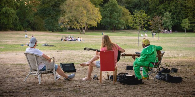 Drei Männer sitzen in einem Park und musizieren