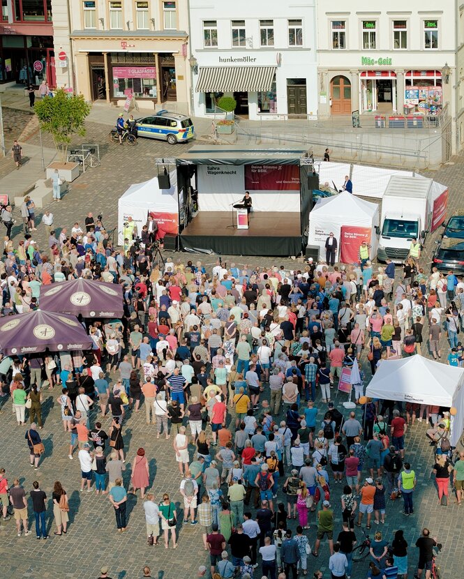 Ein Marktplatz mit vielen Menschen und einem Wahlkampfstand aus der Vogelperspektive