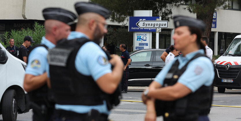 Drei Polizisten stehen vor einem Schild, das zur Synagoge weist