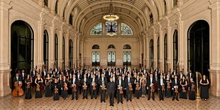 Sehr viele Musiker*innen im strengen schwarzen Outfit stehen zum Fototermin nebeneinander