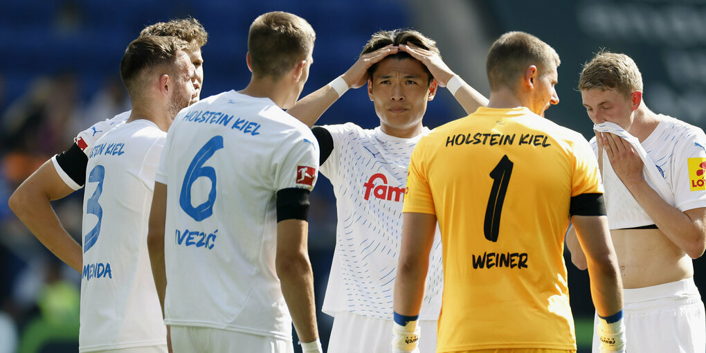 Einige Spieler der Fußballmannschaft Holstein Kiel stehen im Kreis und schauen etwas betrübt