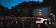 Menschen sitzen in einem Freiluftkino, auf der Leinwand ein Antifa Lobo