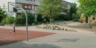 Ein Kind spielt auf einem Basketballplatz vor einem Schulgebäude