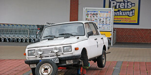 Ein Auto der Marke Wartburg steht aufgebockt vor einem Supermarkt