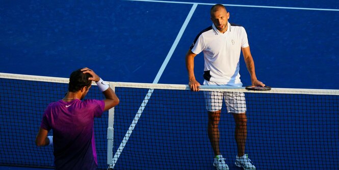 Zwei Tennisspieler stehen sich erschöpft gegenüber, zwischen ihnen das Netz