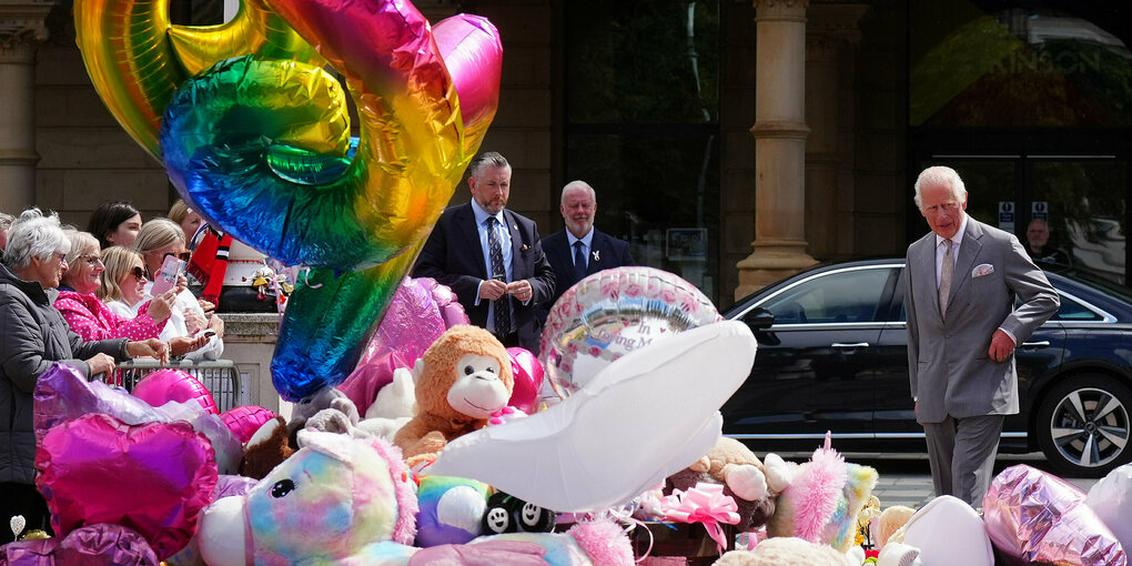 König Charles schaut sich die abgelegten Kuscheltiere und Luftballons vor dem Rathaus an