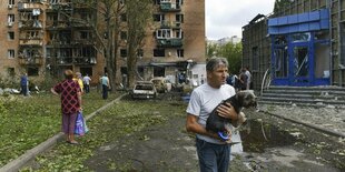 Ein Mann läuft mit einem Hund aus dem Bild, im Hintergrund ist ein Wohnhaus zu sehen