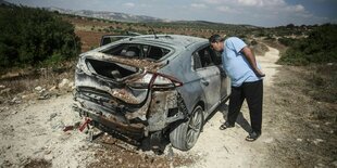 Ein Mann blickt in ein von einer Bombe zerstörtes Auto