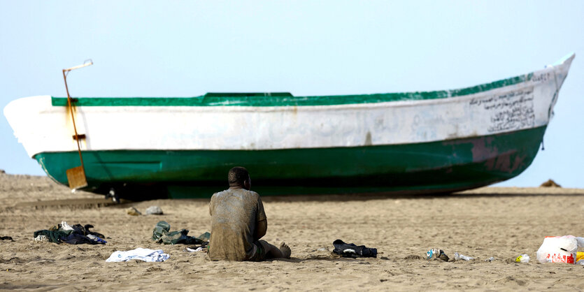 Ein Migrant ruht auf dem Sand neben dem Faserboot, mit dem er auf Gran Canaria ankam