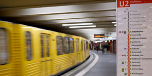 Eine gelbe U-Bahn fährt links im Bild, rechts ist eine Tafel mit den Haltestellen der U2 zu sehen