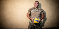 Ein Mann in Militäroutfit hält einen Volleyball in den Händen und lächelt in die Kamera