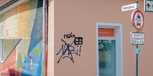 An einem kleinen alt-rosa gestrichenen Haus prangt ein Graffiti: Nazi, das Wort hat jemand durchgestrichen und ein nein dazu gesprayt