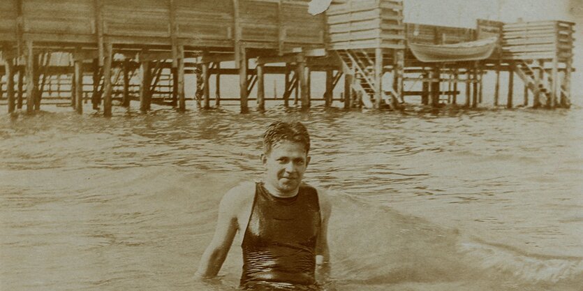 Kurt Tucholsky sitzt im Wasser vor einer Seebrücke.