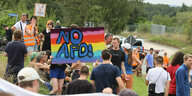 Demonstranten sitzen und stehen auf einer hügeligen Wiese. Einer trägt ein Schild: No AFD