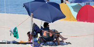 Zwei Menschen liegen unter einem Sonnenschirm an einem Strand