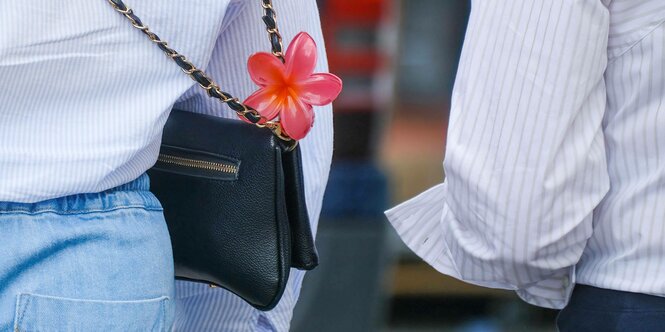 Eine Frau trägt eine Handtasche mit einer Blume geschmückt