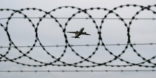 Ein Flugzeug startet - fotografiert durch Stacheldraht am Flughafenzaun