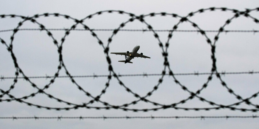 Ein Flugzeug startet - fotografiert durch Stacheldraht am Flughafenzaun