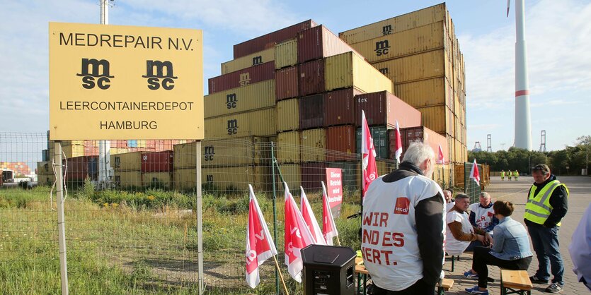 Männer mit Streikwesten, auf denen steht "Weil wir es wert sind" vor eimem Containerberg, im Vordergrund ein Schild der Firma Medrepair/MSC